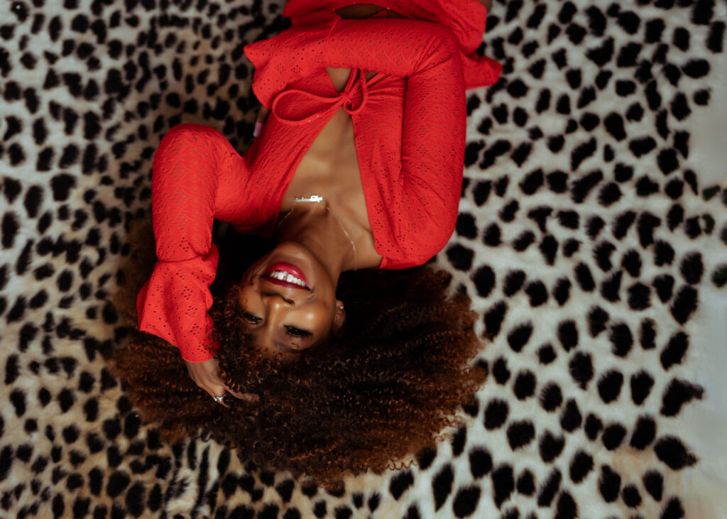 Smiling black woman during boudoir session wearing red lingerie laying on cheetah print rug